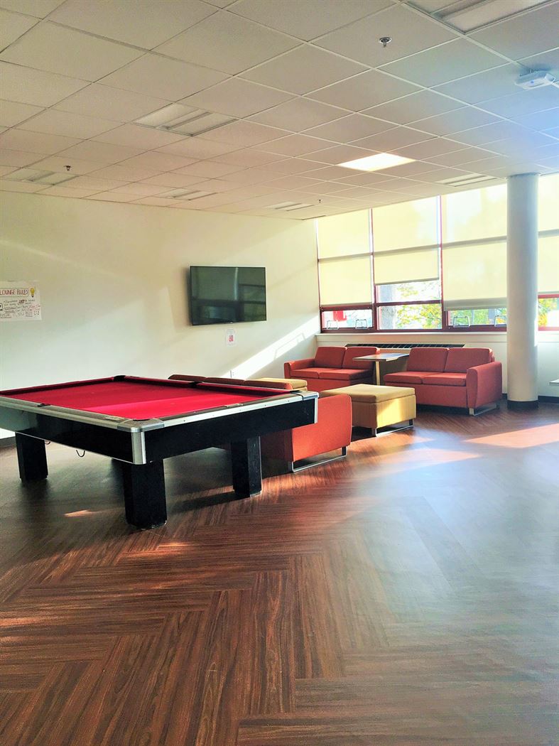 The renovated lounge of Stone Hall, featuring a pool table, multiple flat-screen TVs, hardwood flooring and comfortable furniture. Photo by Kendall Sellinger 