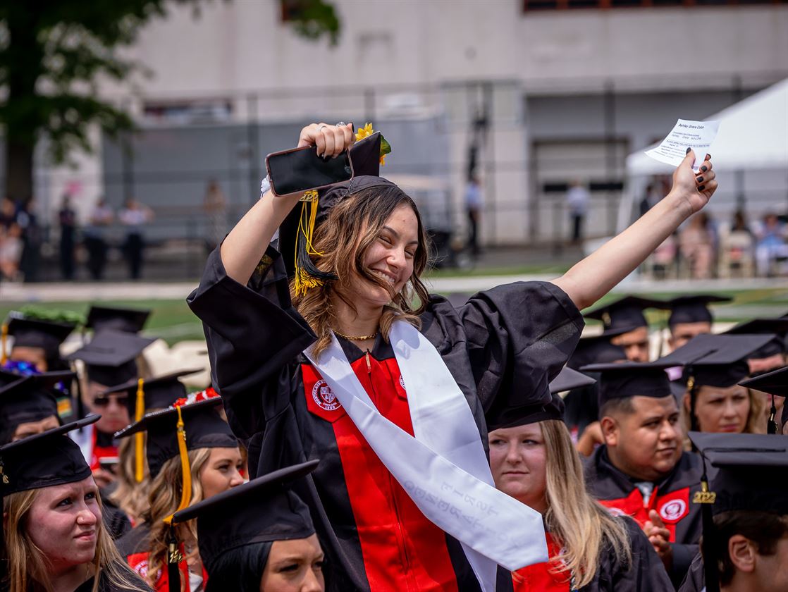 A graduate throws her hands up in the air in celebration.