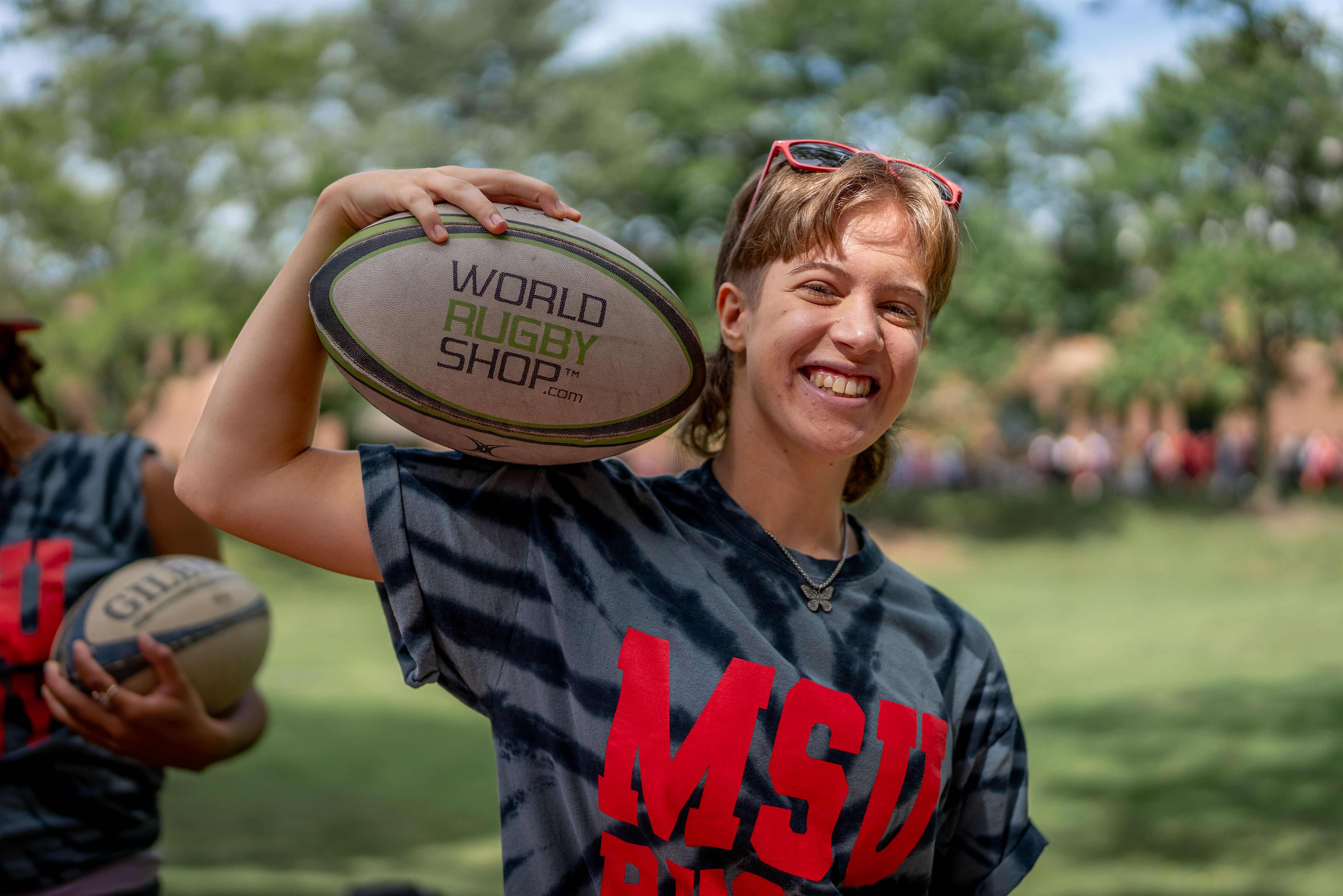Mia Pedalino, a sophomore marketing major, holds up a rugby ball behind the Montclair State Club Rugby table at Red Hawk Day, Tuesday, August 29th, 2023.