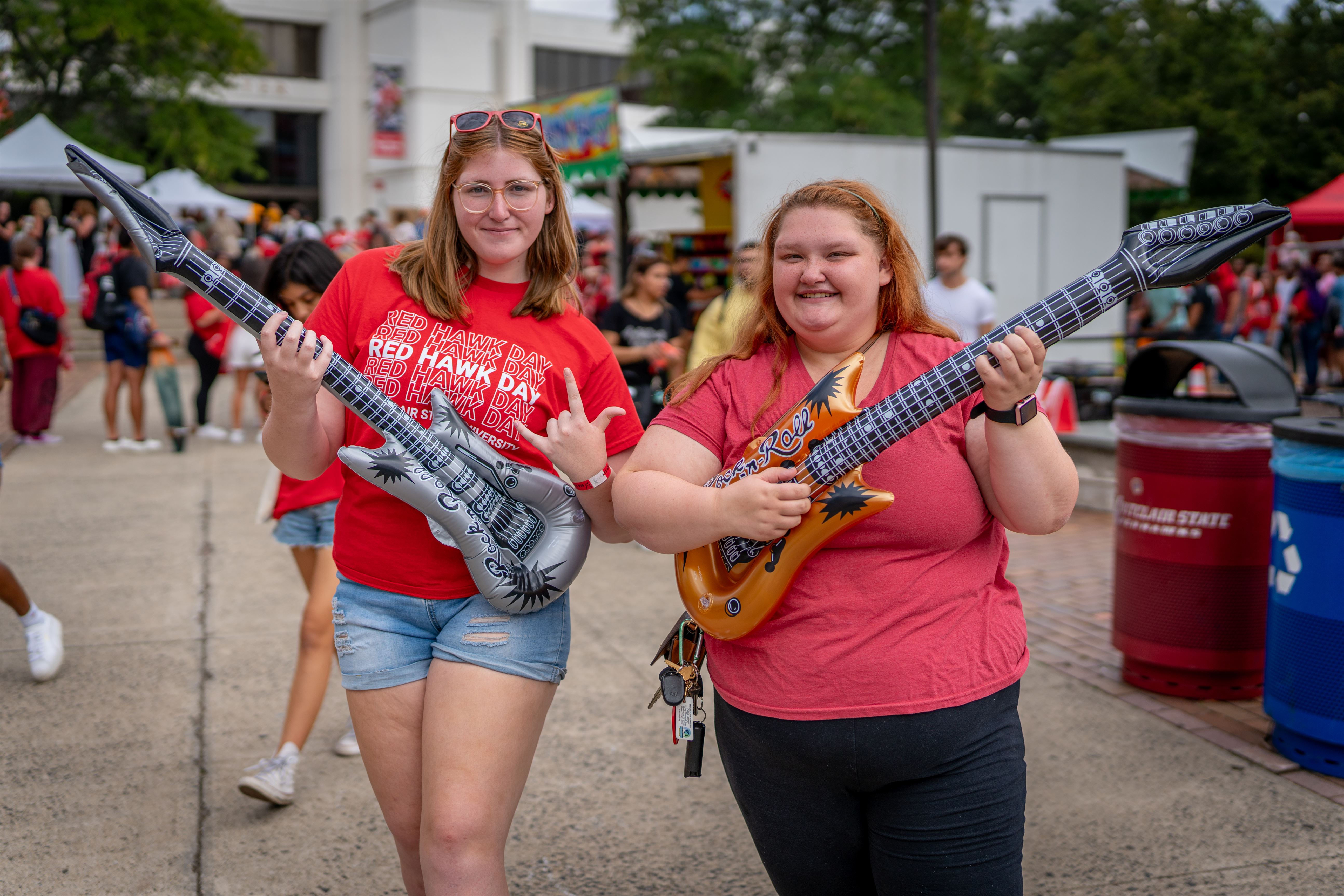 Alyssa Seger, a freshman theater studies major, and Morgan Burns, a freshman history major, show off their inflatable guitars from one of the games at Red Hawk Day, Tuesday, August 29th, 2023.