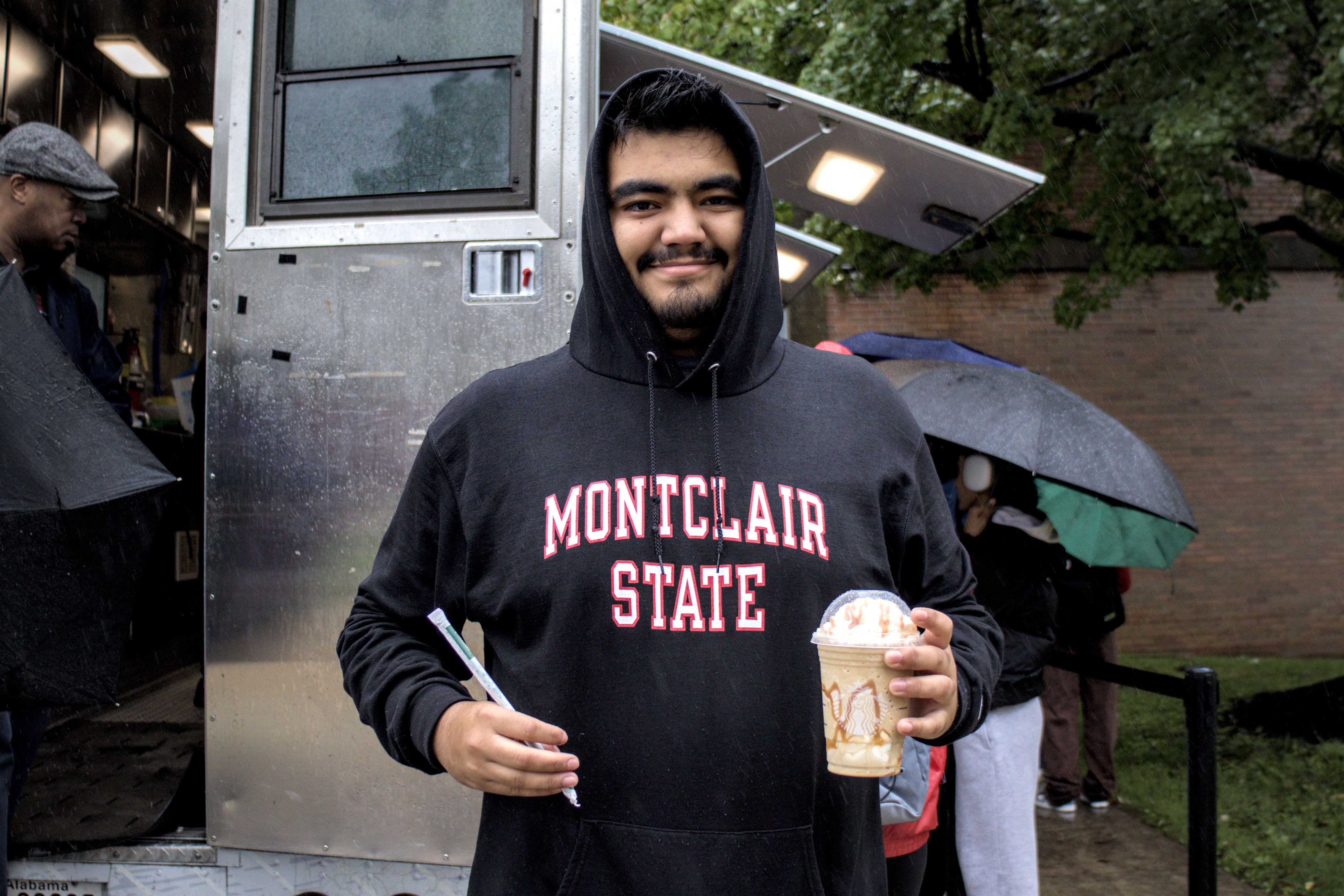 Tall person with black hair tucked into a black and red Montclair State hoodie holds a straw and a Starbucks beverage.