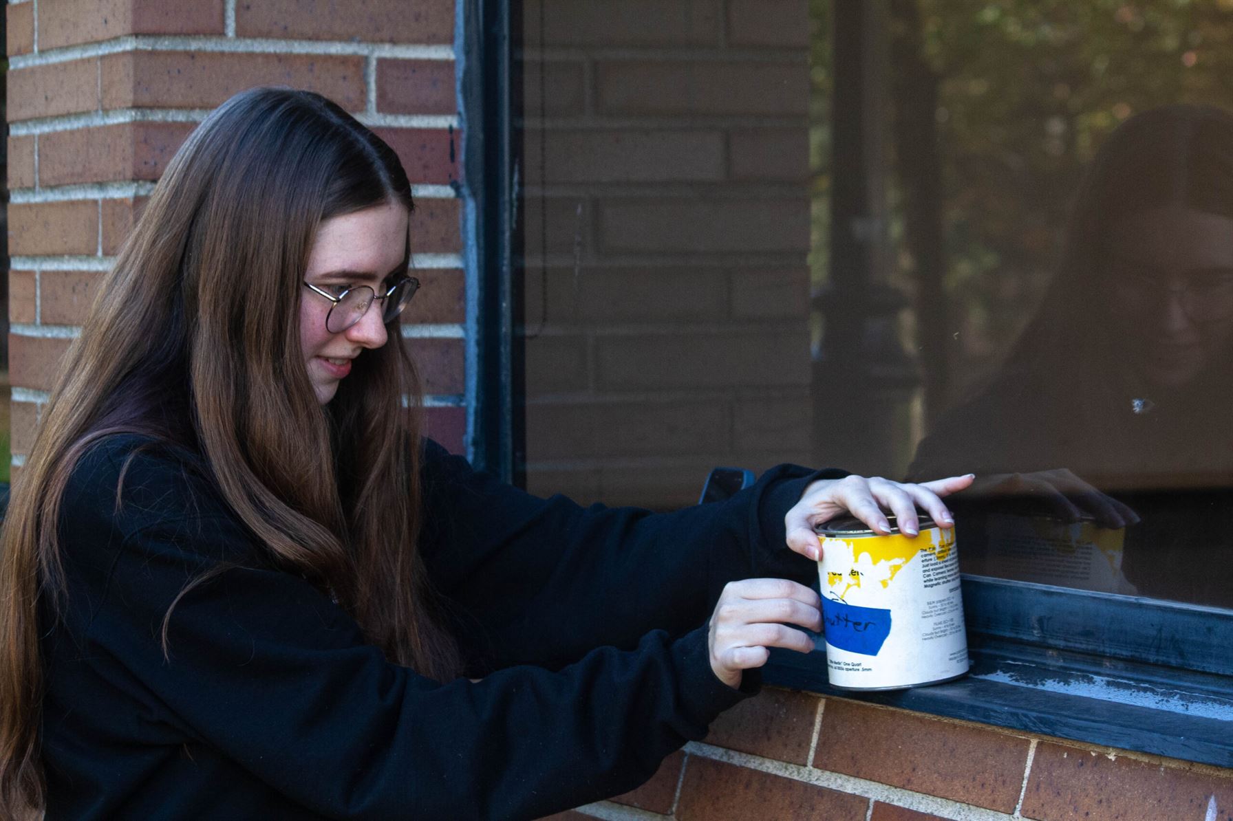 Evans places her paint can on a window sill and peels the tape off of the hole. Photo courtesy of Angel Santos