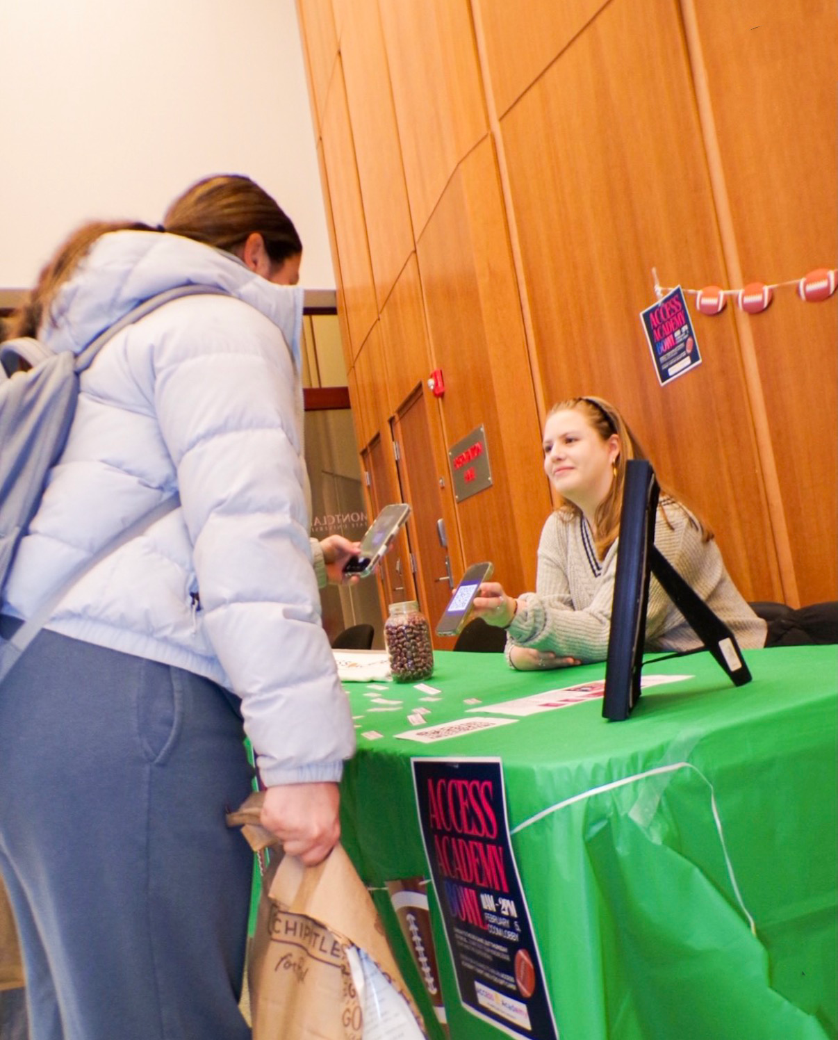 The "ACCESS Academy" team hosted a Super Bowl tabling event for students to learn more about the campaign. Team member Riley Silvester (&squot;26) holds up a QR code for students to guess how many footballs were in the jar for a chance to win a prize.  Credit: Sarah Potter