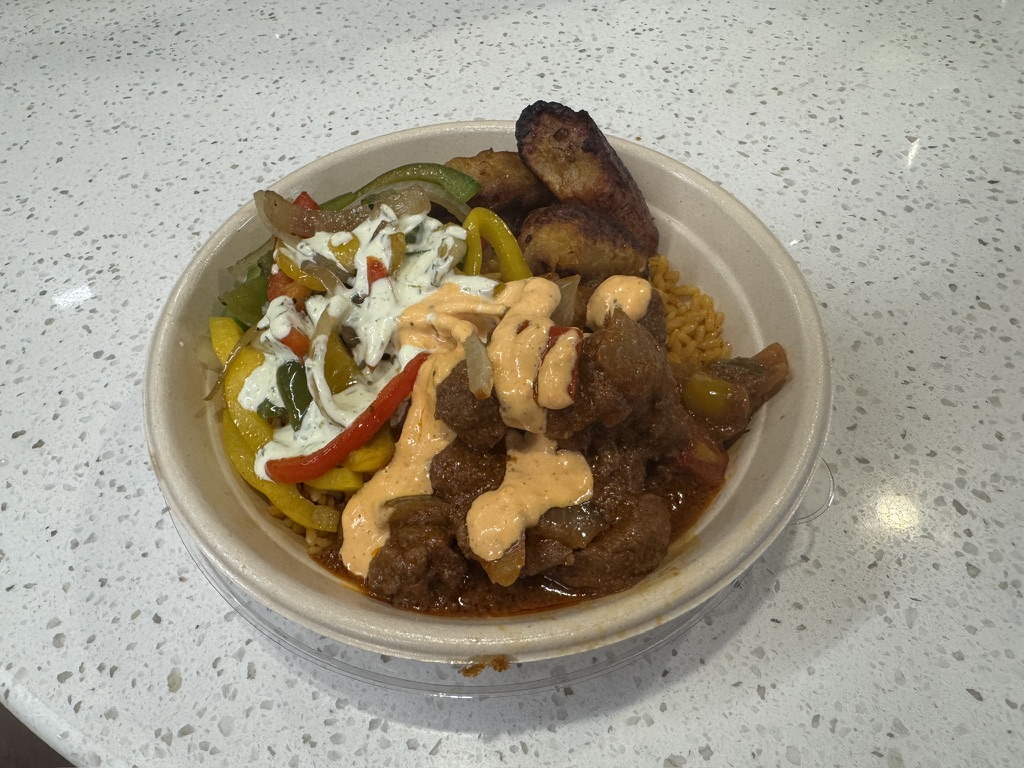 Jollof rice bowl with beef stew and fried sweet plantains, peppers, and onions.