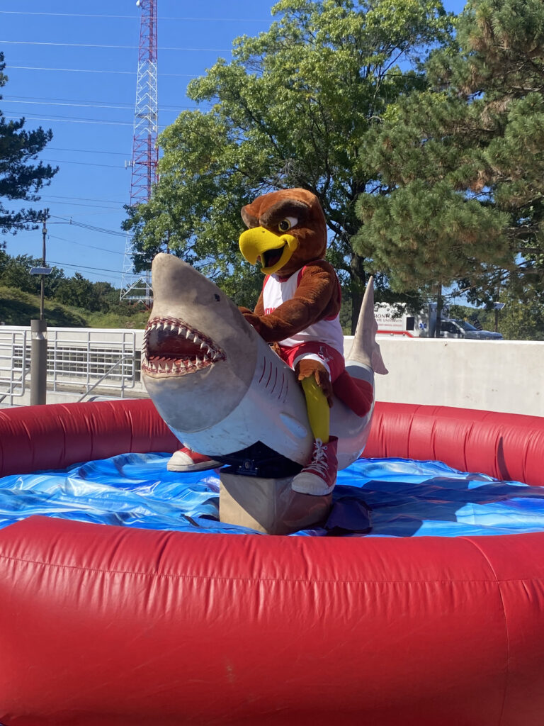 Rocky the Red Hawk takes a ride on a mechanical shark at YouBelong Fest.
Madison Clemente | The Montclarion